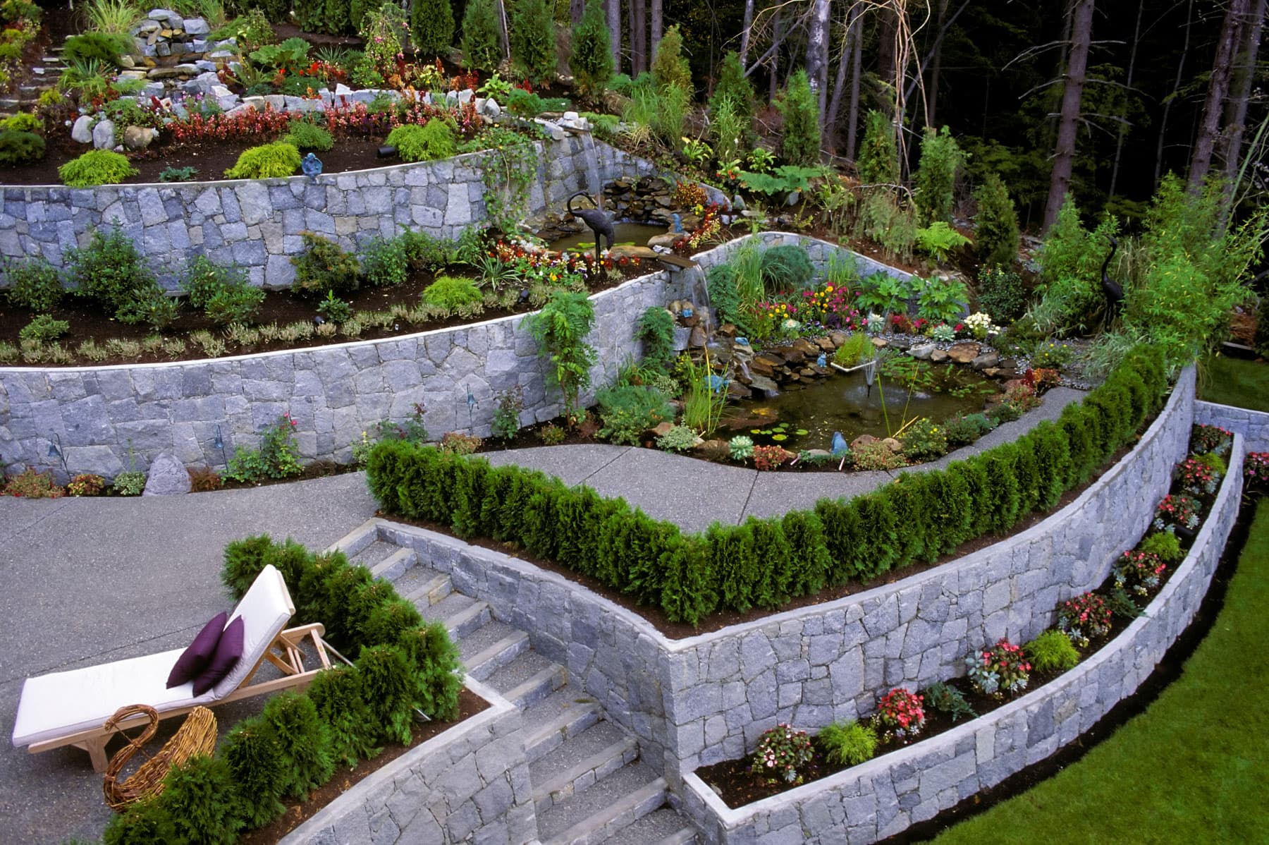 Tiered natural stone retaining walls on a sloped BC property with garden terraces, ponds, and stairs